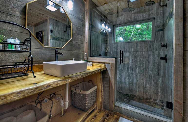 bathroom with wooden walls, tiles that look like the rest of the walls, glass shower, wooden cabinet with the white sink and a mirror above