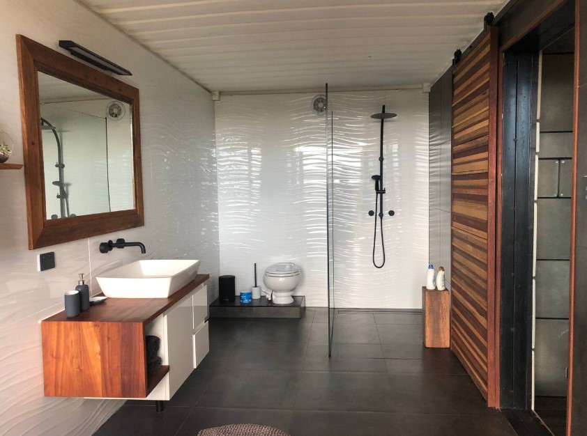 bathroom with a walk in shower, large mirror, brown countertop, white sink