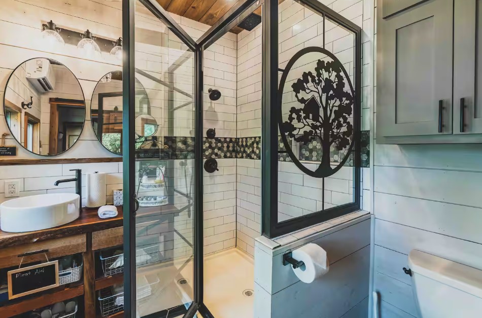 bathroom with a glass shower with art on it, round mirrors, white sinks