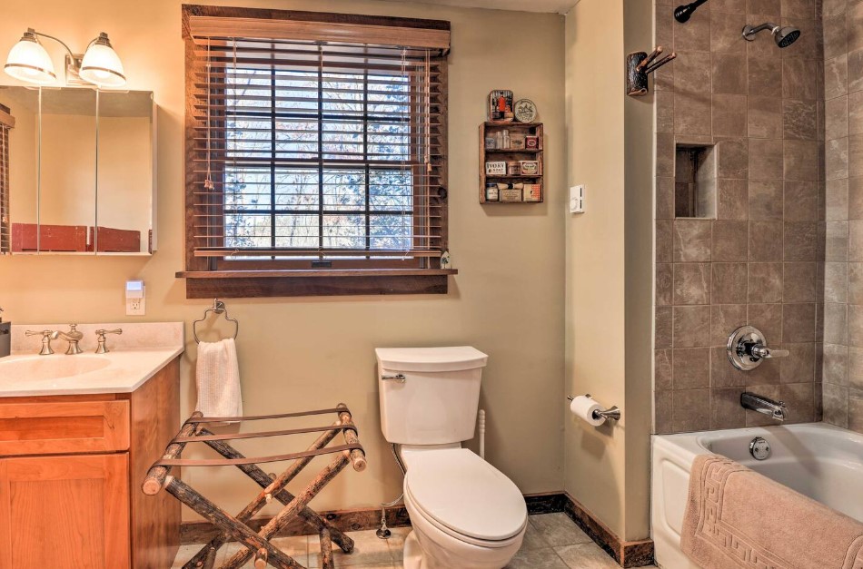 bathroom with a white bathtub, brown earth toned tiles in the shower, tiny wooden shelf on the wall, wooden cabinet