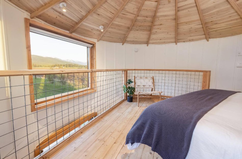 bedroom with a wooden ceiling, big bed, wooden chair, plant, window opposite the bed