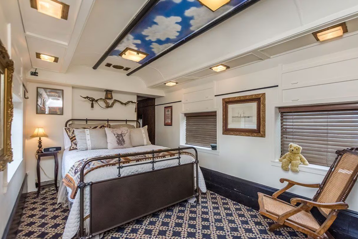 bedroom with a wrought iron bed frames, chair in the corner, ceiling with a sky and clouds mural