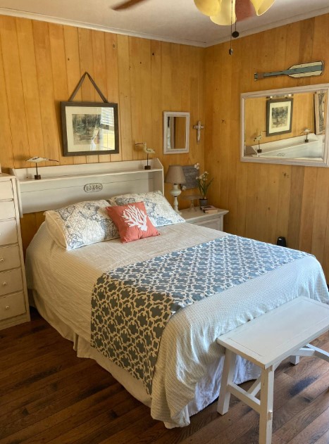 bedroom with a mirror, bed with light bed sheets, wooden walls