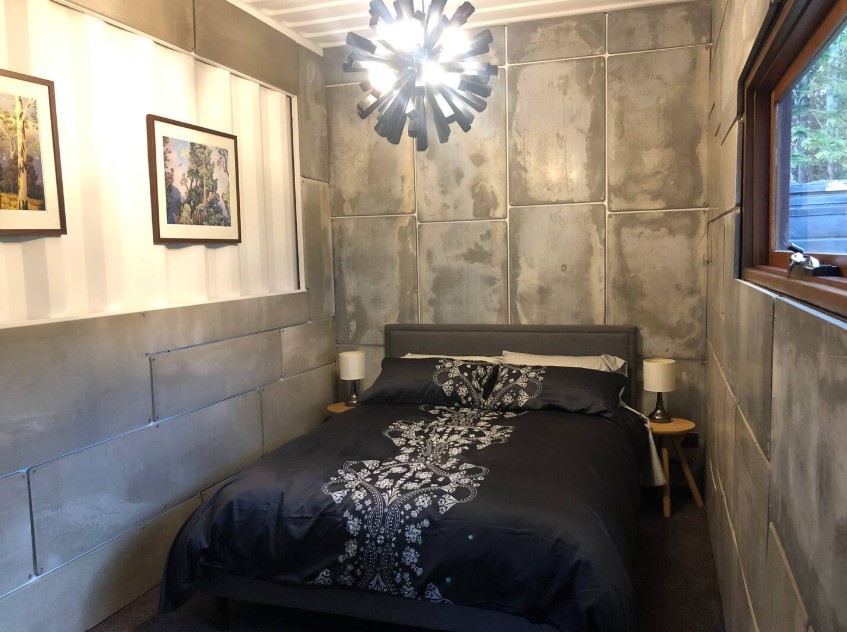 bedroom with gray and white walls, unique chandelier, black and white bed sheets, framed photos