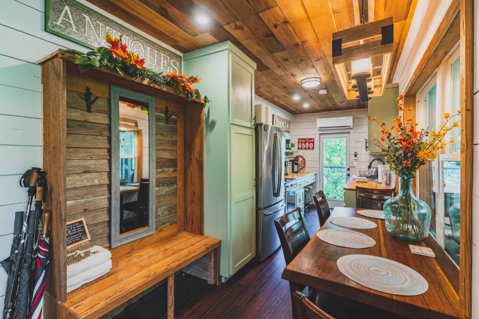 brown dining table with flowers on top, kitchen in the back with mint cabinets