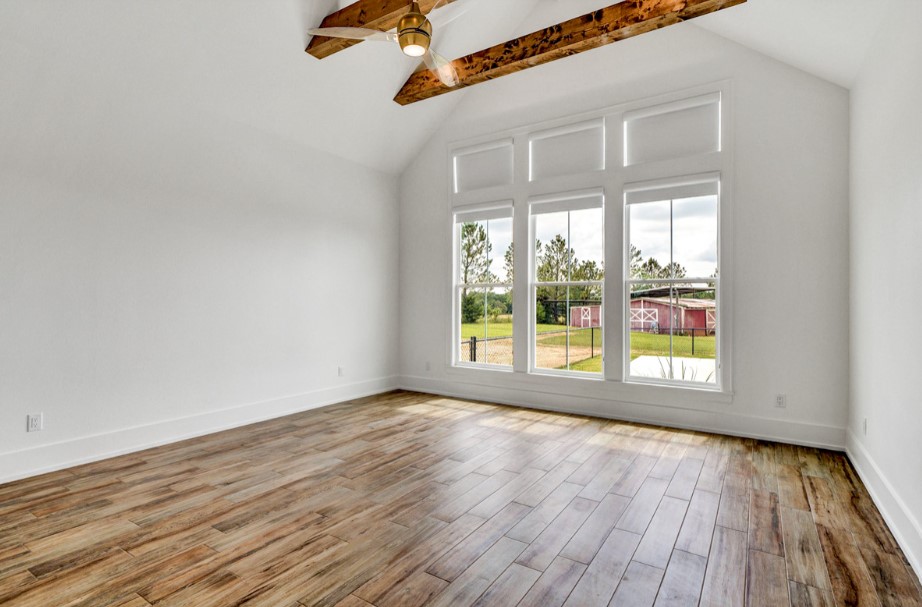 empty bedroom with large windows, white walls and wooden beams