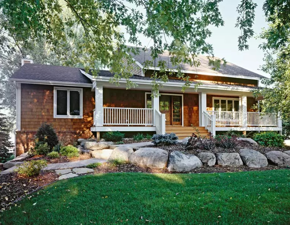 exterior of a home with a porch and white fence in front, big stones on the lawn