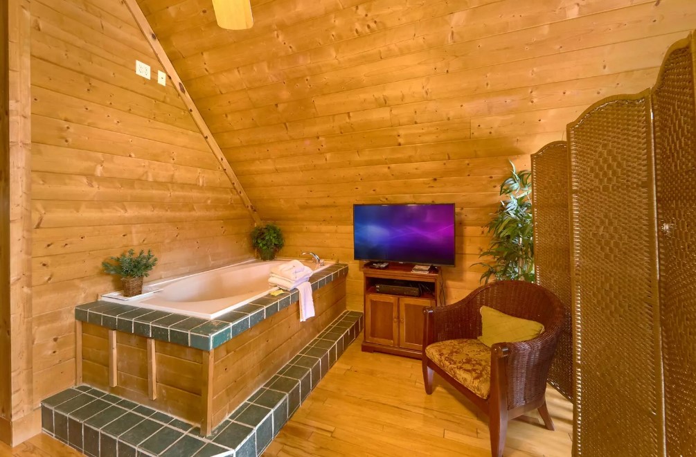 a bathtub with a flat screen tv in front and a brown chair