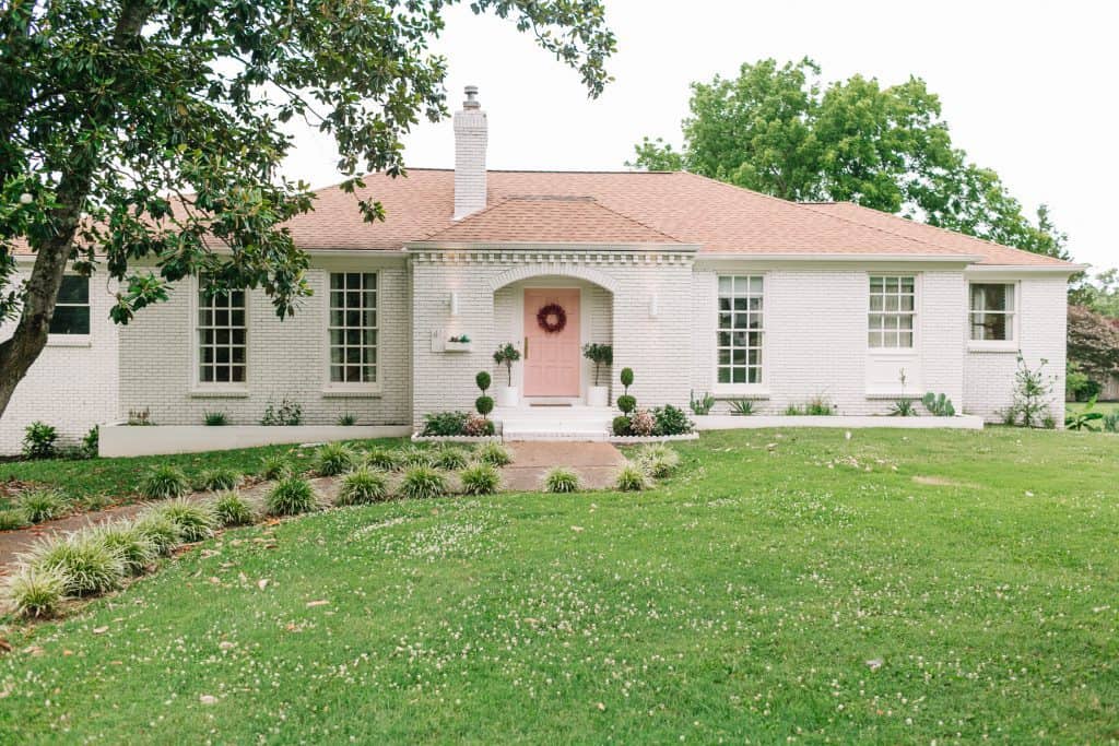 exterior of a home with white exterior, light pink doors and tiny bushes in front