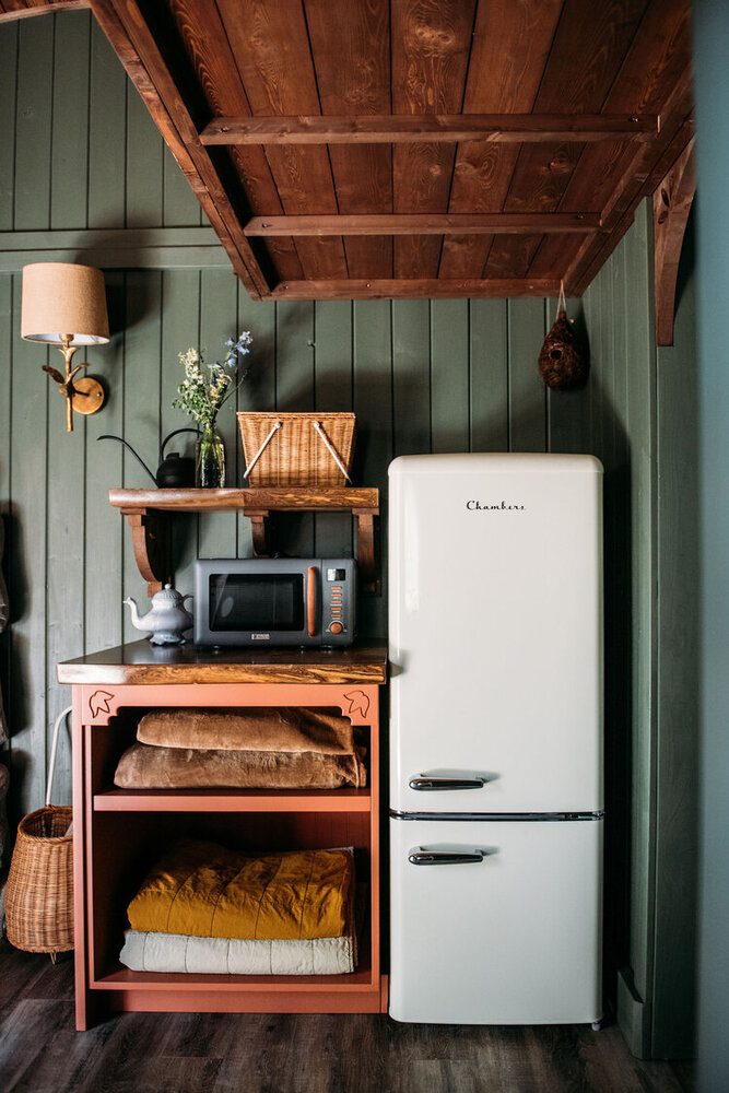 mini kitchen with a white fridge, brown open cabinet and a microwave