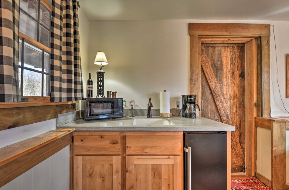 kitchenette with wooden cabinets and white walls, checkered curtains on a window