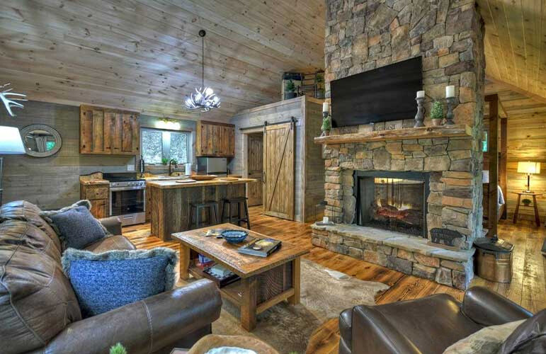 living room with a brown leather couch, flat screen tv, fireplace with stone around, wooden table