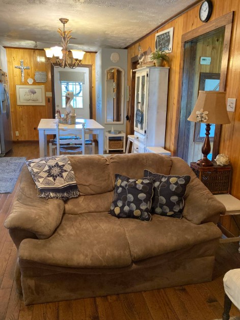 living room with a brown couch, dining room with a farmhouse style with a white table and chairs in the background