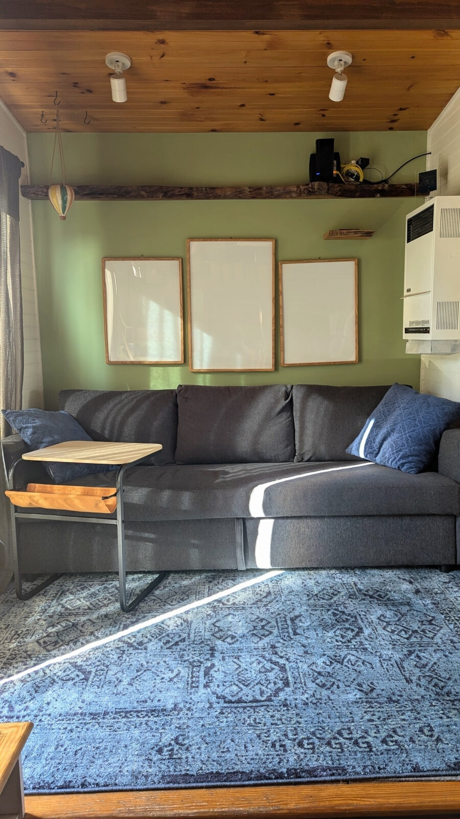 living room with a dark gray couch, blue carpet, frames above the couch, one green wall, wooden ceiling