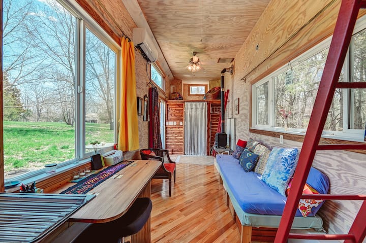 living room with a built in couch with blue cushions, colorful pillows, wooden desk, large windows