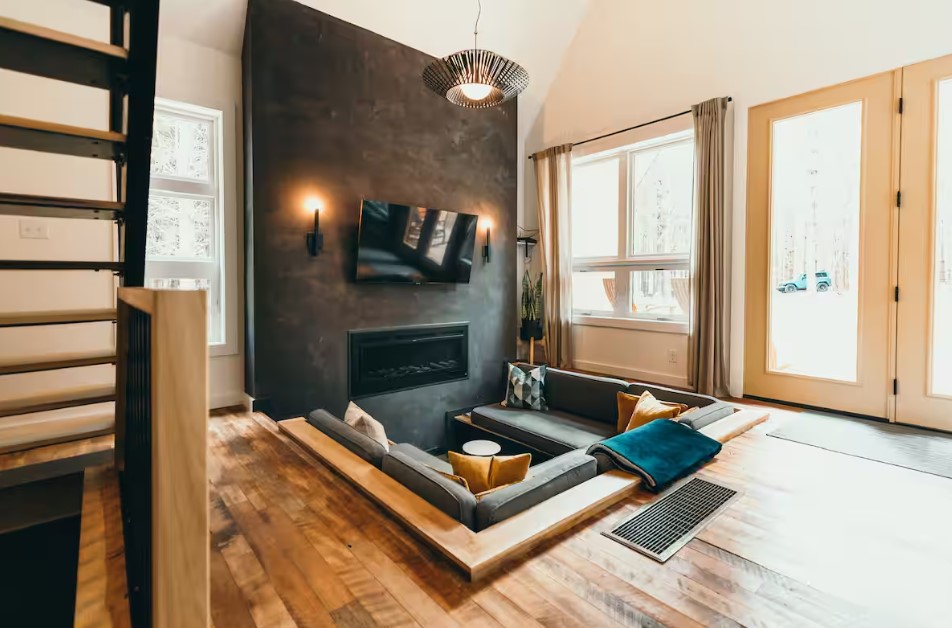 living room with sunken down sitting area, flat screen tv, black accent wall, big windows, fireplace