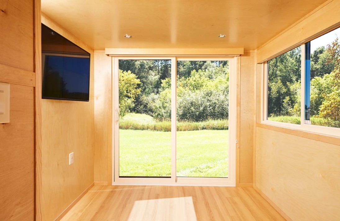 empty living room space with light brown walls, large windows, glass sliding doors, flat screen tv