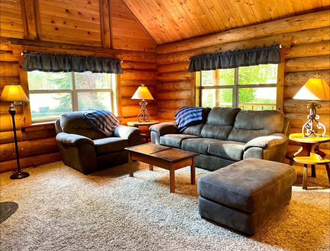 living room with a gray couch, two windows, wooden table, wooden walls