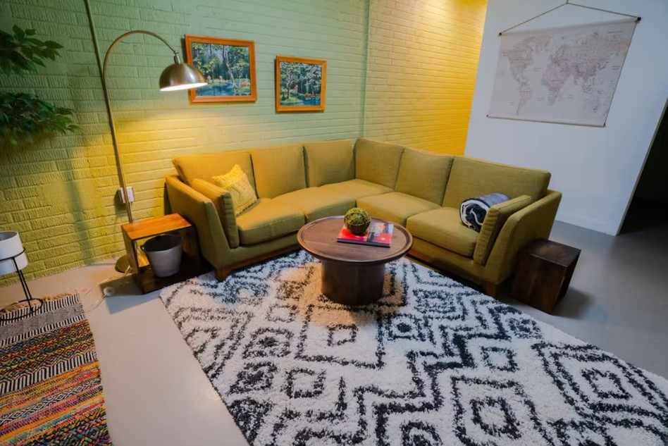 living room with an l-shaped green couch, patterned carpet, round brown table