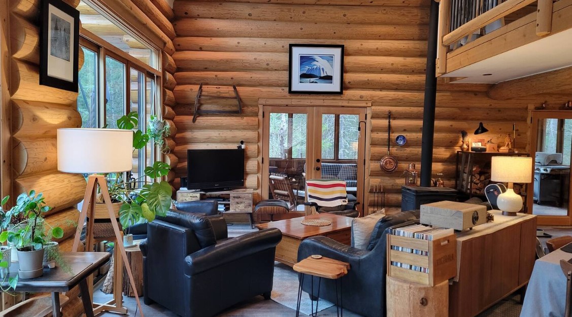 living room with leather black couches, brown cabinet with a record played and records, flat screen tv, big windows, wooden walls