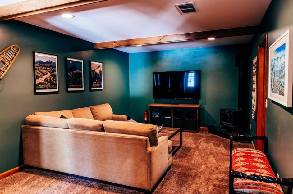 living room with an l-shaped couch, dark green walls, flat screen tv, framed landscapes