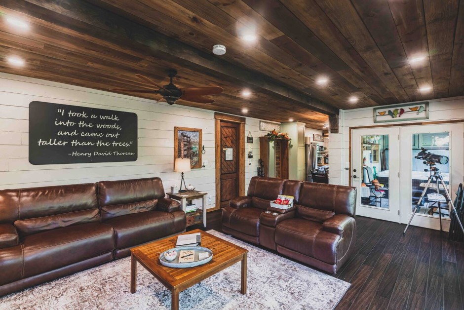 living room with leather brown couches, wooden table in the middle, brown wooden ceiling, white walls, telescope