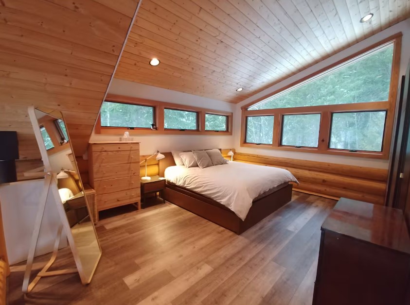 loft bedroom with a king sized bed, windows, brown cabinets and a tall mirror