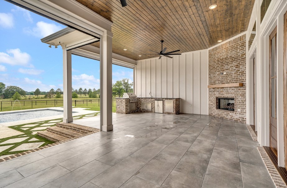 patio of a farmhouse with an l-shaped countertop, grill, pool, fireplace