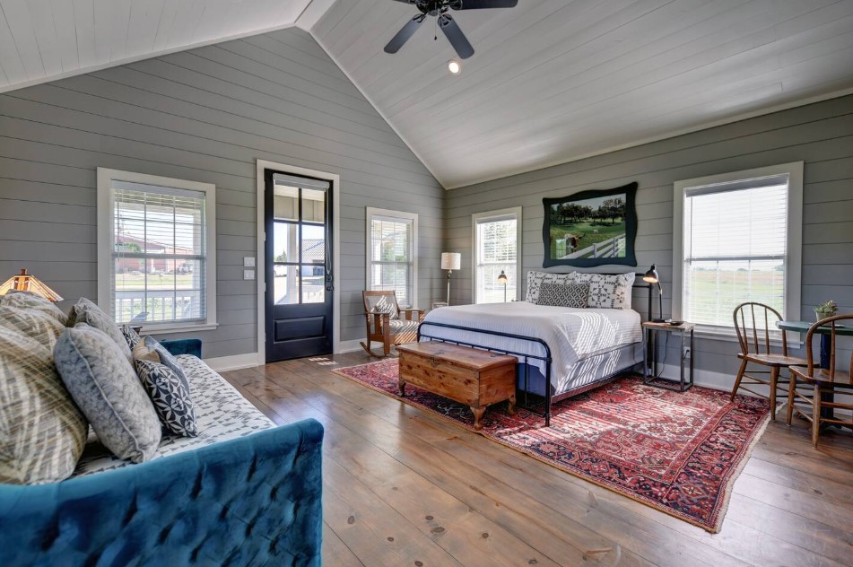 room with a queen-sized bed with a brown cabinet at the bottom, rocking chair in the corner, blue couch, windows on the walls