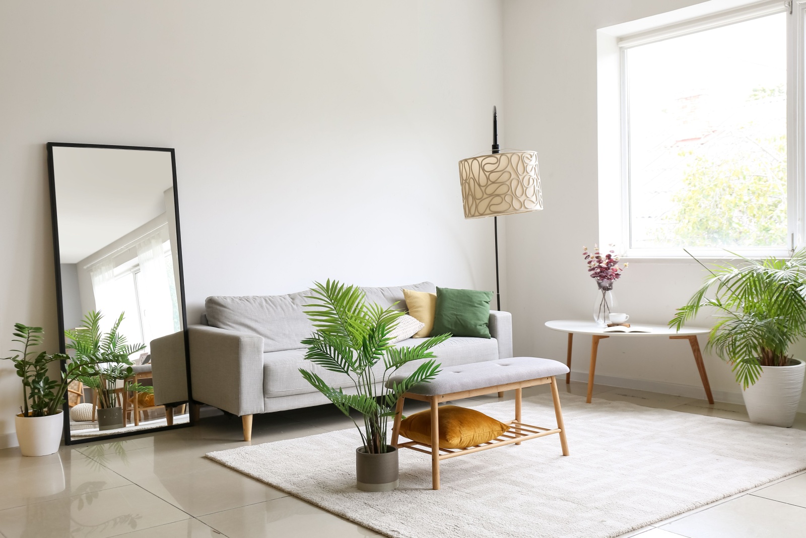 living room with a tall mirror, gray couch, white table and a big window