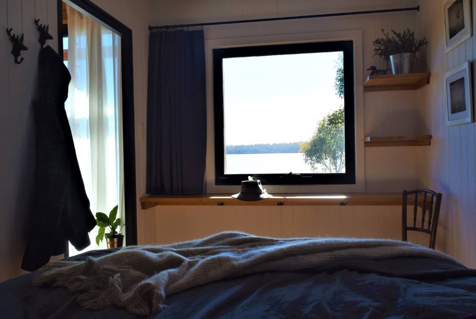 bedroom with a bed, window opposite the bed, built in table and shelves