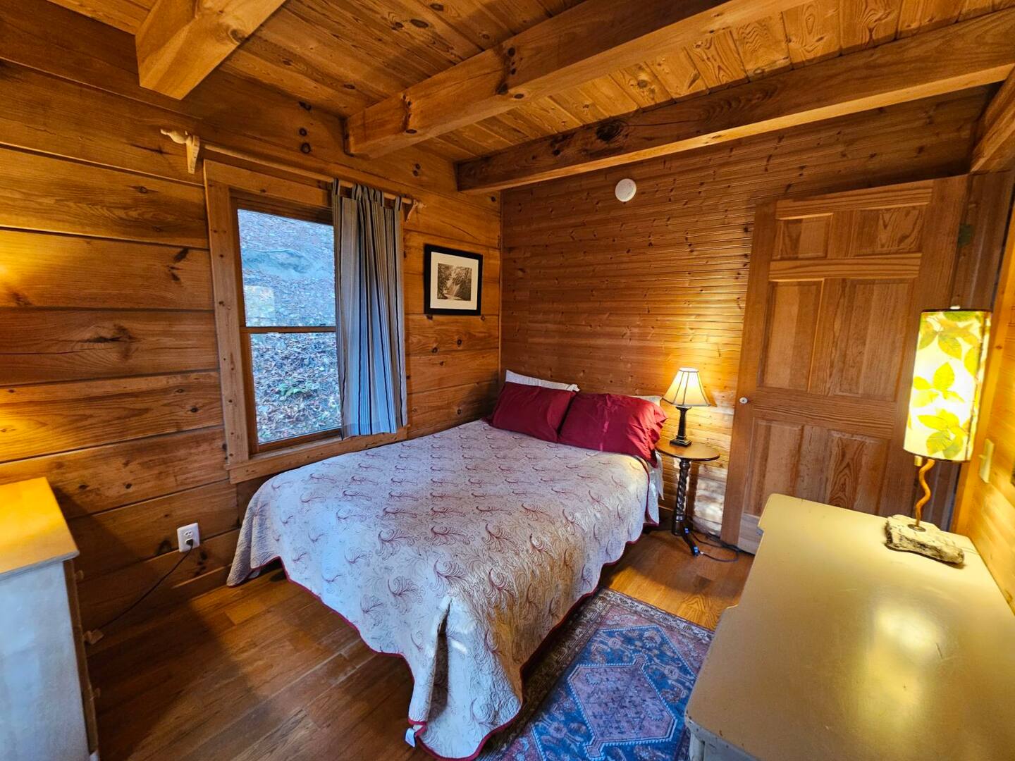 bedroom with a bed next to the window, wooden walls, bedside table with a lamp