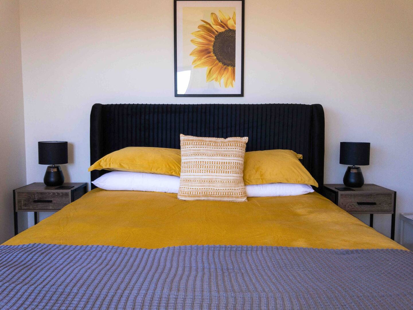 bedroom with a black bed frame, brown bedside tables, sunflower art piece above the bed