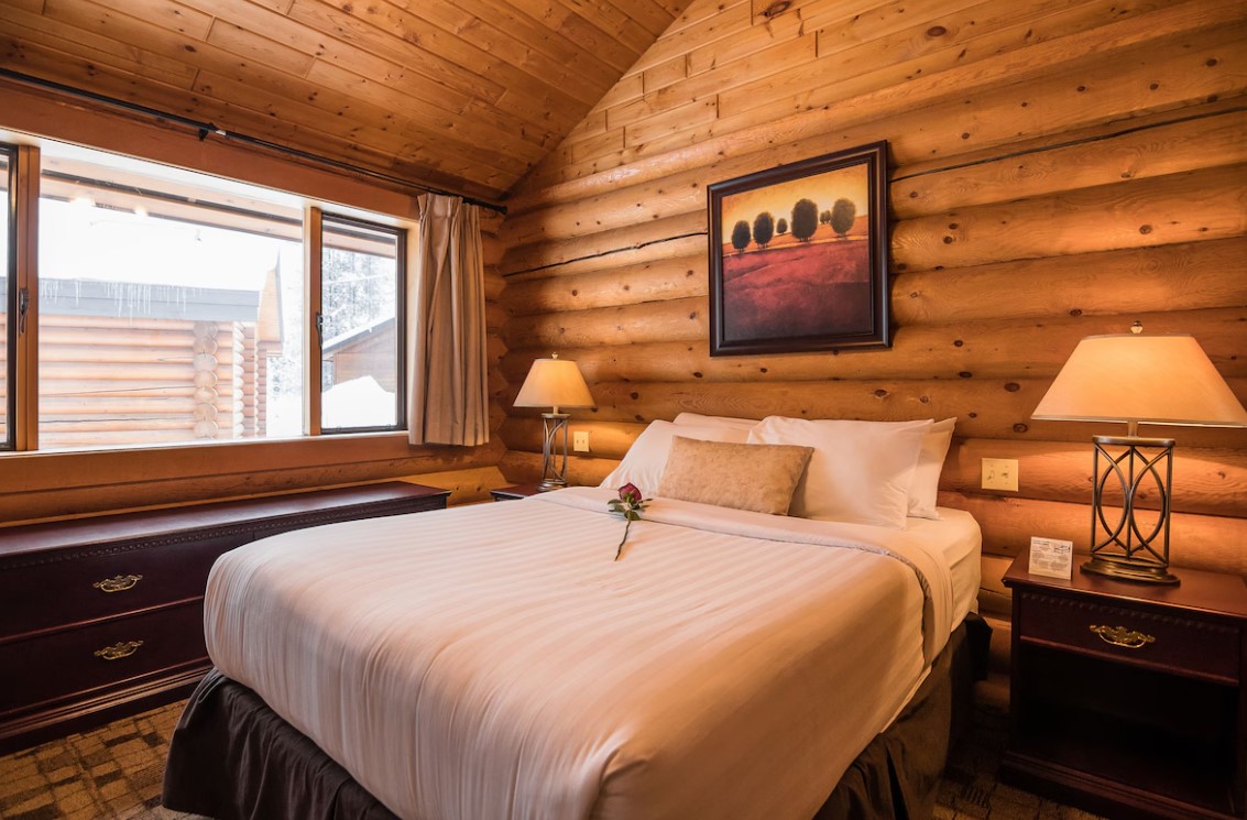 bedroom with log walls, comfy bed, lamps on bedside tables, big window