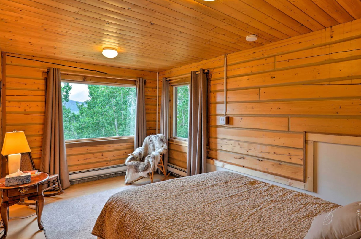 bedroom with big windows, bed, chair with a blanket over her, round table