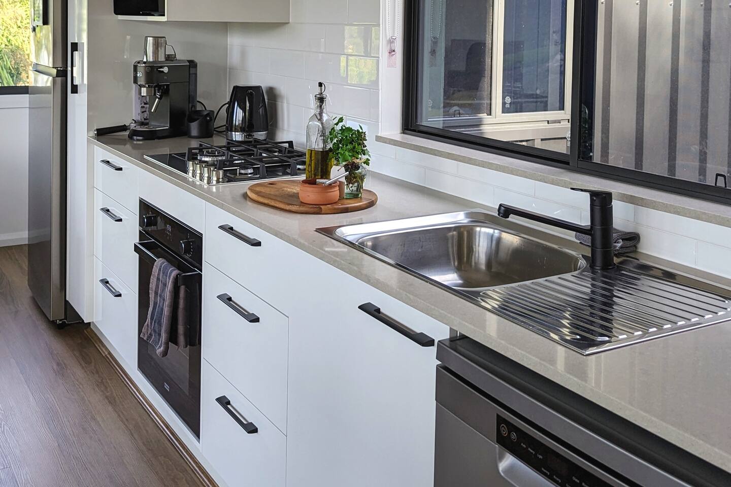 kitchen with white cabinets, black handles, big window above the gray countertop