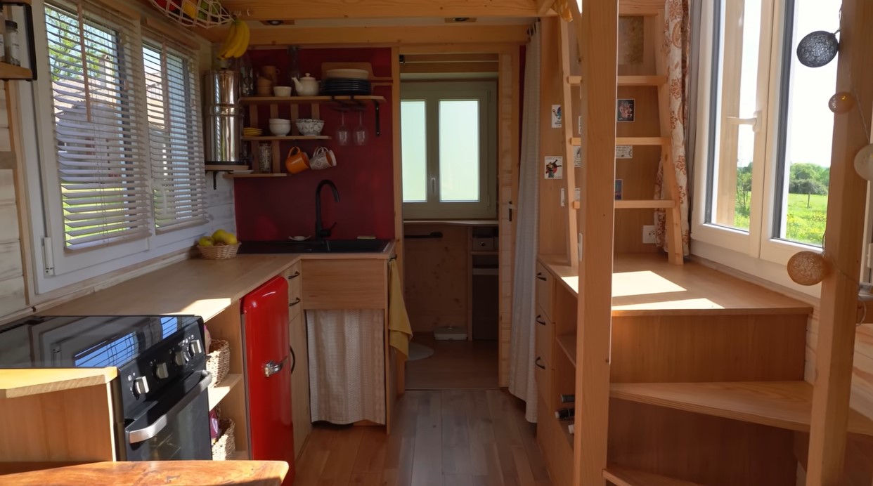 kitchen with wooden cabinets, red fridge, red accent wall, windows above the countertops