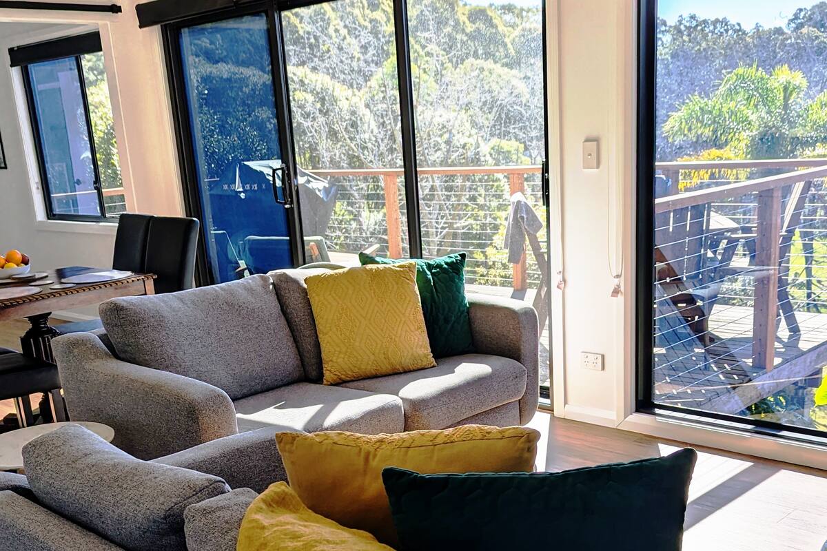 living room with gray couches, mustard yellow and green pillows and a deck outside