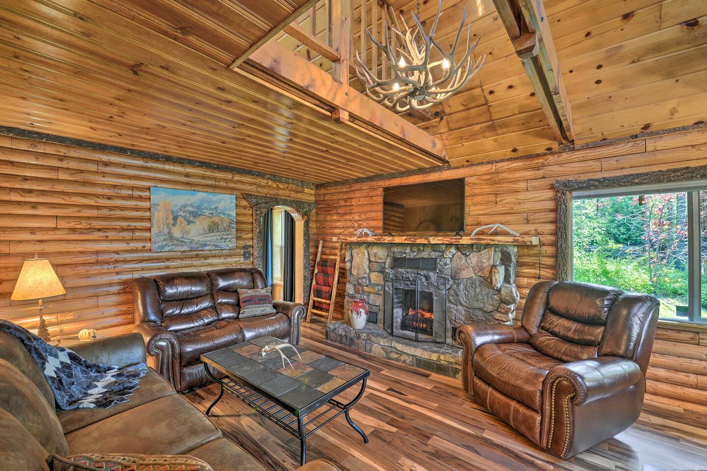 living room with log walls, leather sofas, flat screen tv, stone fireplace