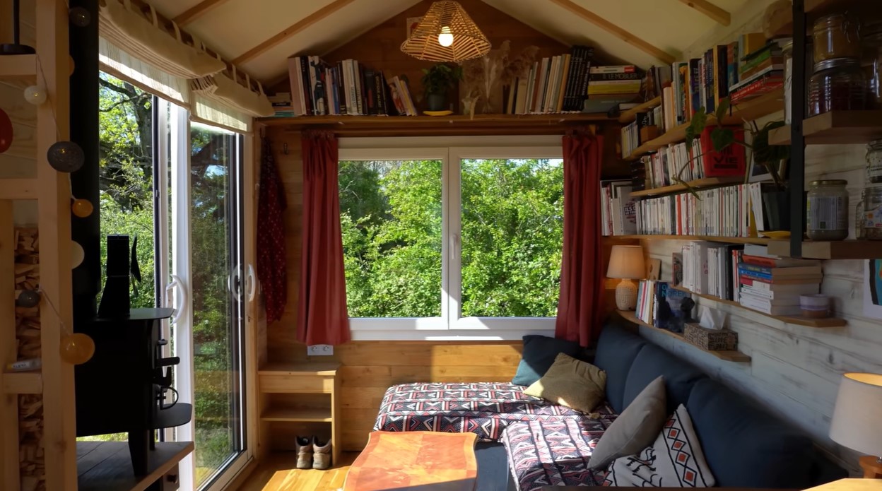 living room with a window and glass doors, a lot of shelves with books, a sectional and a wooden table