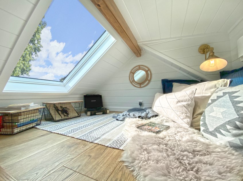 loft with a skylight, baskets with books and records, comfy furniture, white walls